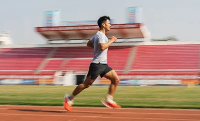 Fotobehang Gymnastiek A man is motion blurred running around an outdoor track showcasing athletic speed and fitness  © Q88