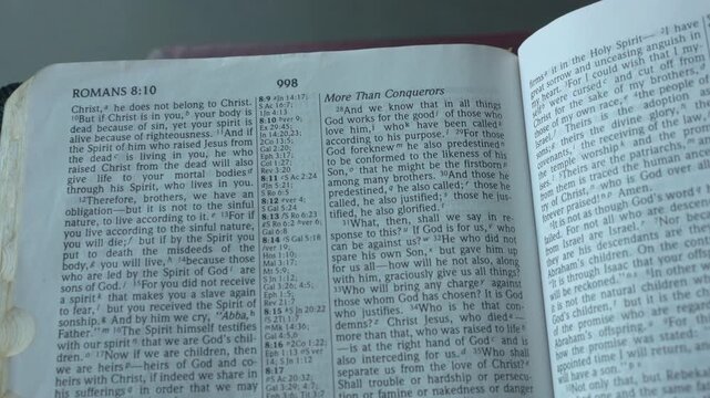 Holy Bible open up to the book of Romans of the new testament, zooming into Chapter 8 verse 28. New International Version.