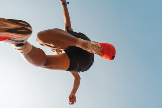 Dynamic low angle of runner mid-air in athletic shoes against clear blue sky action capture