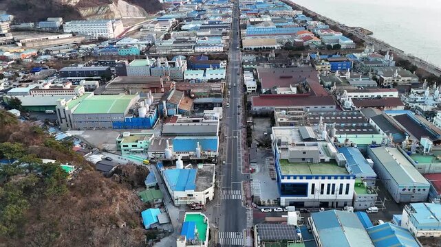 Drone aerial footage of industrial district in coastal city factories warehouses road along sea dense buildings urbanization environmental concept South Korea