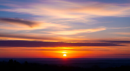Fototapeta premium Vivid sunrise paints the sky with fiery hues, casting a warm glow over the tranquil landscape at dawn