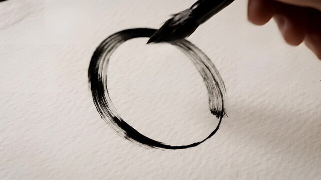 Closeup of a hand painting a black circle with a brush on paper.