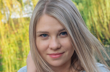 Naklejka premium Headshot of a young woman with straight light blonde hair and blue eyes outdoors in natural light