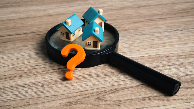 Real estate market search concept with miniature houses and a question mark placed on a magnifying glass lens