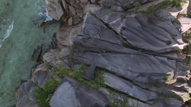 4K drone footage showing an aerial reveal of massive granite boulders, lush greenery, and turquoise waters at Anse Grosse Roche beach, La Digue island, Seychelles 014 30fps