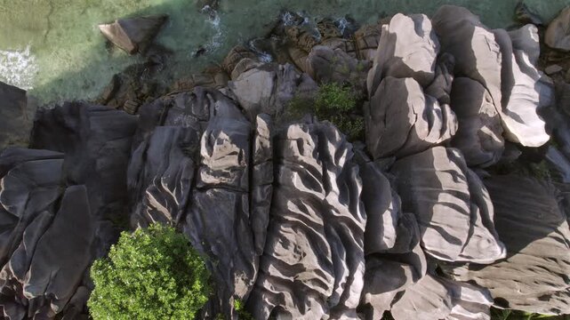 Dramatic aerial pull-up showing ancient granite boulders meeting crystal clear turquoise waters and lush jungle at Anse Grosse Roche, La Digue, Seychelles 002 30fps