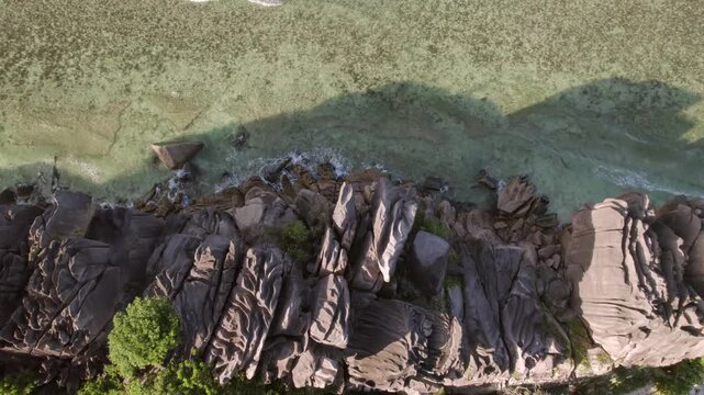 Drone footage captures the rugged granite boulders bordering calm turquoise waters at Anse Grosse Roche, La Digue, Seychelles 003 30fps