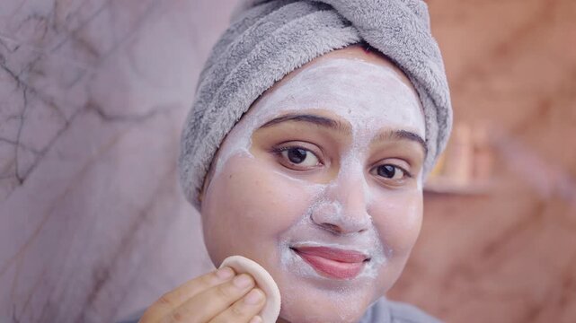 Close up shot of a woman wiping off facial mask using a cotton pad in indoor setting.