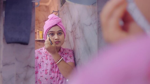 Young female shaping eyebrows with eyebrow pencil in front of a bathroom mirror during daily beauty routine.