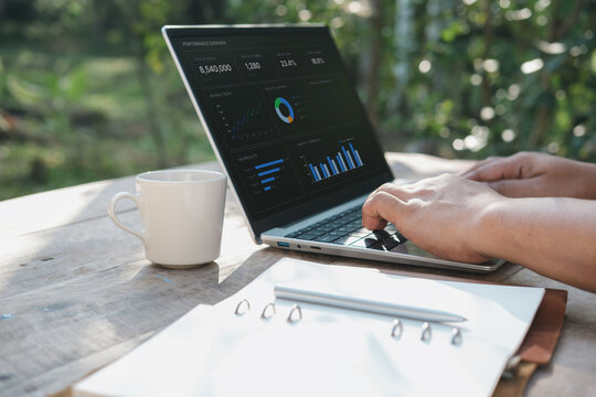 Remote work productivity concept with hands typing on laptop showing business analytics dashboard on wooden desk with coffee and notebook in natural morning light outdoor workspace