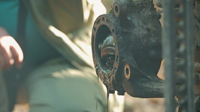 Close up mechanic working on dirty, greasy SUV axle. Shallow depth of field focuses on oily part, highlighting gritty nature of vehicle repair. Natural light illuminates textures