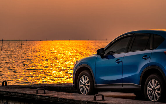 Blue compact SUV parked by sea at sunset, hybrid electric vehicle. Environmentally friendly technology, automotive business concept. Coastal travel lifestyle. Clean energy and sustainable mobility.