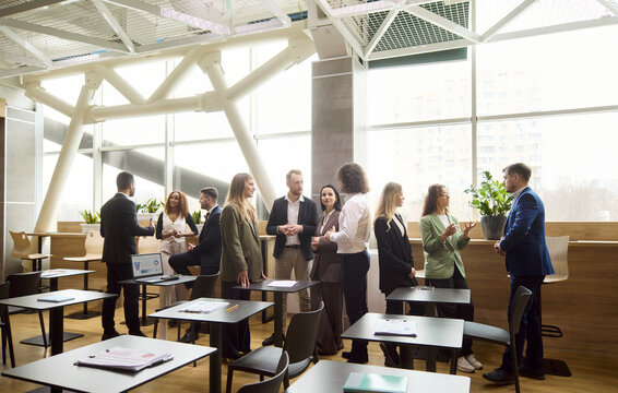 Business professionals team networking in office meeting. Colleagues in groups hold discussion by desks, exchanging ideas during a break. People focus on communication and collaboration.