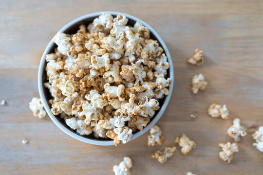 A ceramic bowl overflowing with popcorn on counter, with scattered kernels