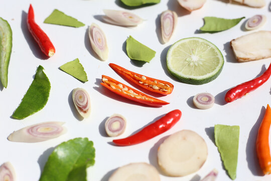 A colorful, close-up pattern of Thai herbs: lime slices, galangal, lemongrass, chilies, and kaffir lime leaves.
