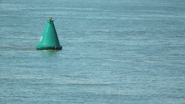 A single green navigation buoy floats in the calm blue waters of the river. A minimalist composition. Conceptualizing safety, navigation, and direction finding