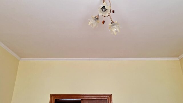Ceiling light with three downward lampshades on metallic base against white ceiling and yellow walls, highlighting simple indoor lighting arrangement with warm glow in a cozy room