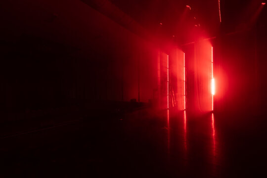 Red lighting illuminates a dark room with smoke, creating a dramatic atmosphere with vertical light strips and reflections on the polished floor surface