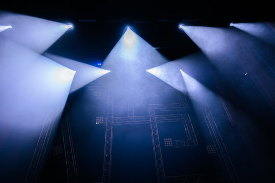 Stage lighting beams illuminate a darkened performance area with smoke effects creating a dramatic atmosphere for concerts and theatrical productions