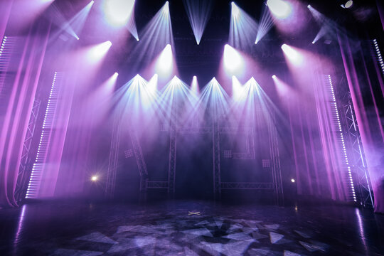 Stage lighting setup with purple and white beams illuminating an empty theater stage, smoke effects creating a dramatic atmosphere for performances and events