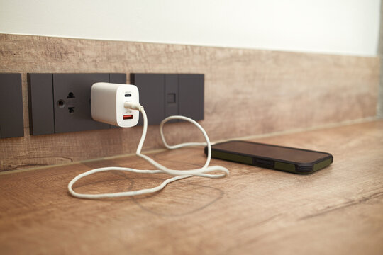 The power outlet is charging a mobile phone that's placed on the table.