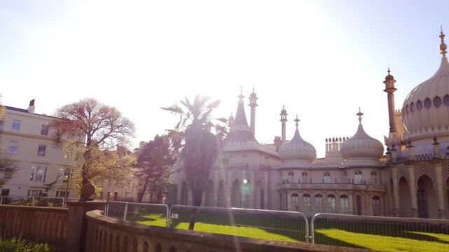 Smooth cinematic left-to-right pan across the Brighton Royal Pavilion. Golden sunlight, palm tree foreground, and intricate domes create a rich architectural travel scene in Brighton, UK.