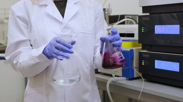 Laboratory environment with technician analyzing red liquid and water a conical flask under bright overhead lighting