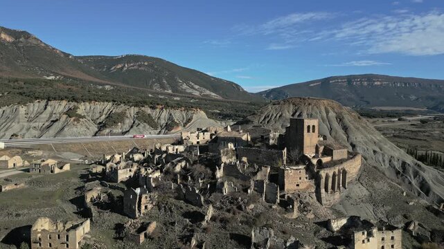 Cinematic aerial perspective of the desolate ghost town of Esco, a historic abandoned village in the Aragon region of Spain, revealing ancient stone ruins and a medieval romanesque church