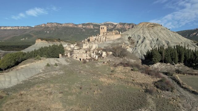 Aerial view of the abandoned Esco town, a ghost town nestled in the Aragonese Pyrenees in Spain, with its crumbling stone houses, old church, and barren hills under a clear blue sky