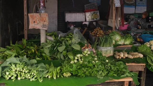 Market stall displaying daikon ginger onion choy sum cabbage long beans thai basil and leafy greens arranged in bundles on traditional Asian vegetable counter. Fresh local produce concept