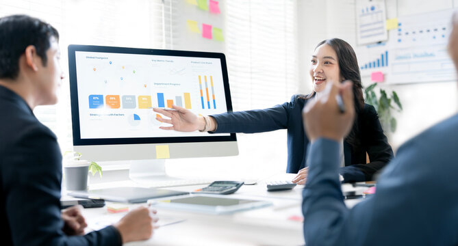 Smiling businesswoman presenting financial charts on a computer monitor to her colleagues during a productive team meeting in the office.