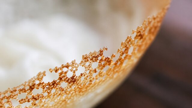 Close-up macro view of a traditional South Indian appam, highlighting its perfectly cooked, crispy, golden brown, lacy, and porous edge, a delicious breakfast delicacy.