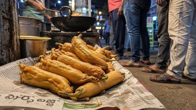 Freshly deep fried spicy chili bajji snacks sit on a sheet of newspaper as a popular evening street food dish being served to local waiting customers