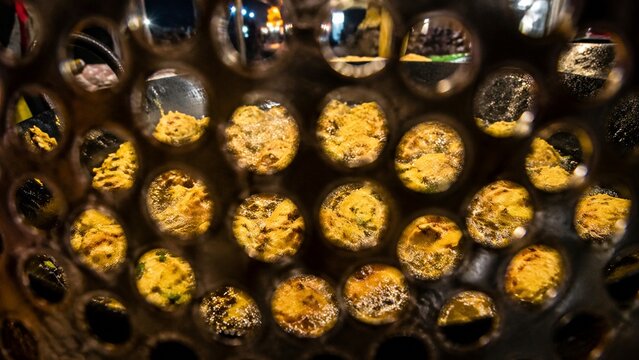 Golden brown food balls frying inside a circular metal sieve viewed through holes during the cooking process tonight
