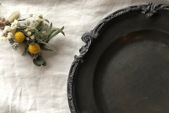 Vintage pewter plate with dried flower bouquet on white linen background copy space