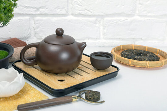 Brown ceramic teapot and cup on bamboo chaban tray for traditional tea ceremony. Pressed pu-erh leaf in bamboo basket. Zen lifestyle, home meditation and healthy herbal drink ritual