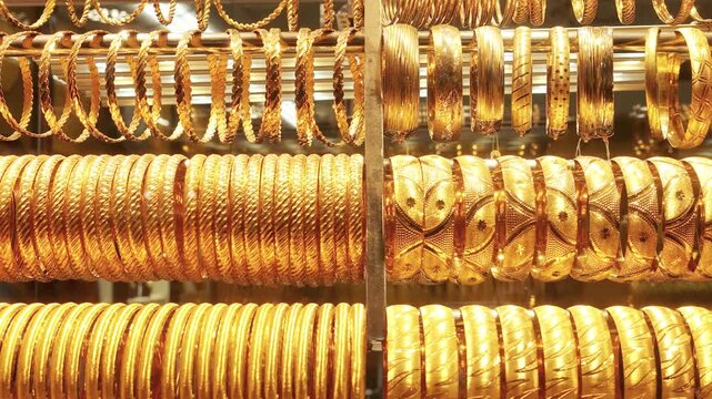 Rows of ornate gold bangles and bracelets shine on display racks in a jewelry shop as the camera slowly pans across the collection