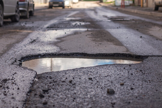 A large pothole filled with water in the middle of the road.