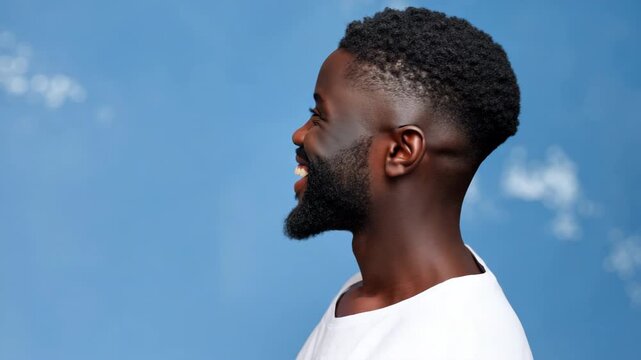 Male african young thoughtful portrait of a young adult man with beard and short haircut wearing a white t shirt against a soft blue backdrop looking contemplative and poised