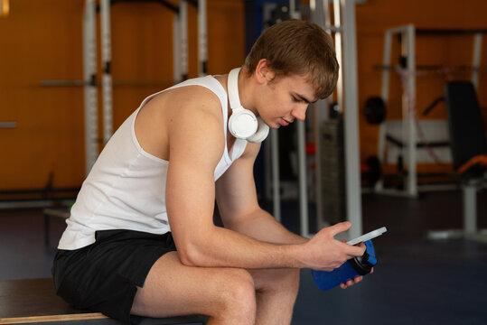 Young sportsman resting in gym with smartphone