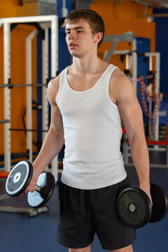Young man lifting weights in gym environment