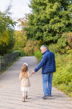 Grandfather and granddaughter walking in a park path happily