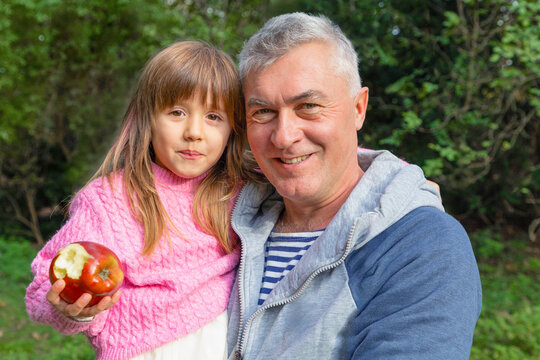 Happy grandfather holding granddaughter with bitten apple