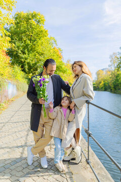 Happy family by riverside with bouquet on sunny autumn day