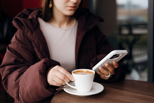 Woman in cafe holding smartphone and drinking coffee