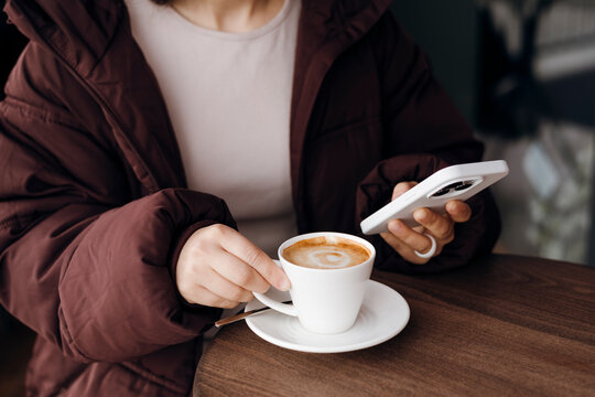 Person using smartphone while holding cappuccino in cafe
