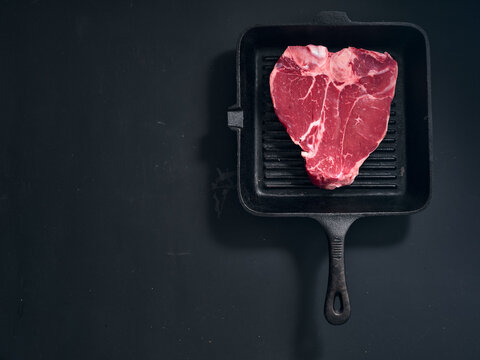 Raw t-bone steak in grill pan on dark surface at home