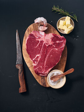 Raw t-bone steak with knife, butter, garlic and herbs