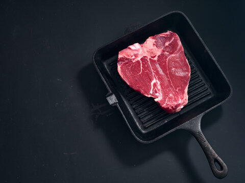 Raw t-bone steak on black cast iron grill pan ready
