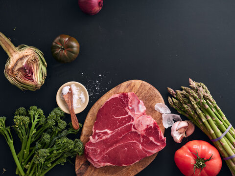 Selecting raw t-bone steak and vegetables in kitchen light